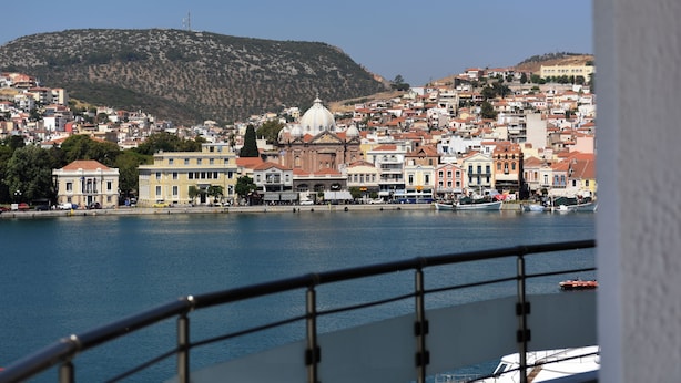 Un paysage urbain côtier avec un bâtiment remarquable surmonté d’un dôme blanc, une colline en arrière-plan et une étendue d’eau au premier plan.