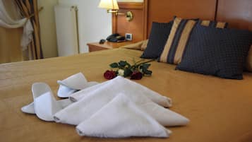 Una cama bien hecha con una colcha marrón, toallas blancas y un ramo de rosas rojas.