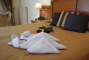 A neatly made bed with a brown bedspread, white towels, and a bouquet of red roses.
