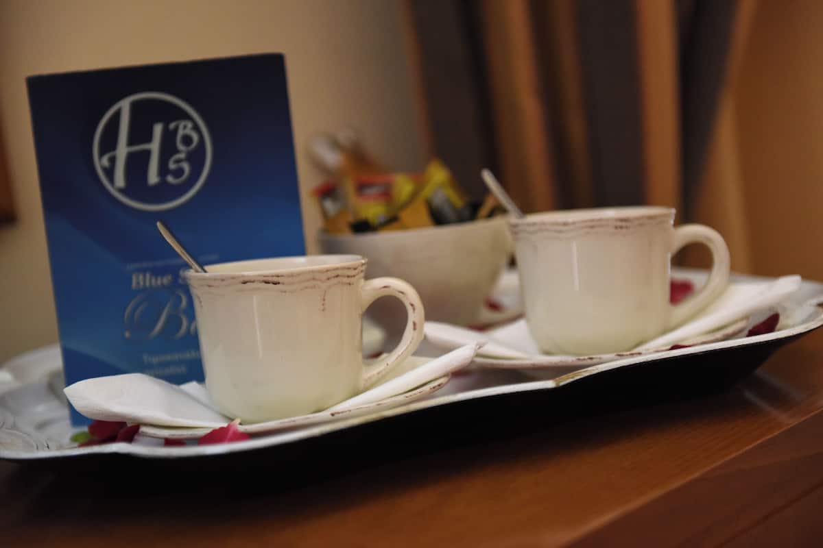 Deux tasses en céramique blanche sont posées sur un plateau, accompagnées d’une cuillère. On aperçoit également un panneau bleu avec le logo « HB5 » et, au fond, un bol rempli d’en-cas.