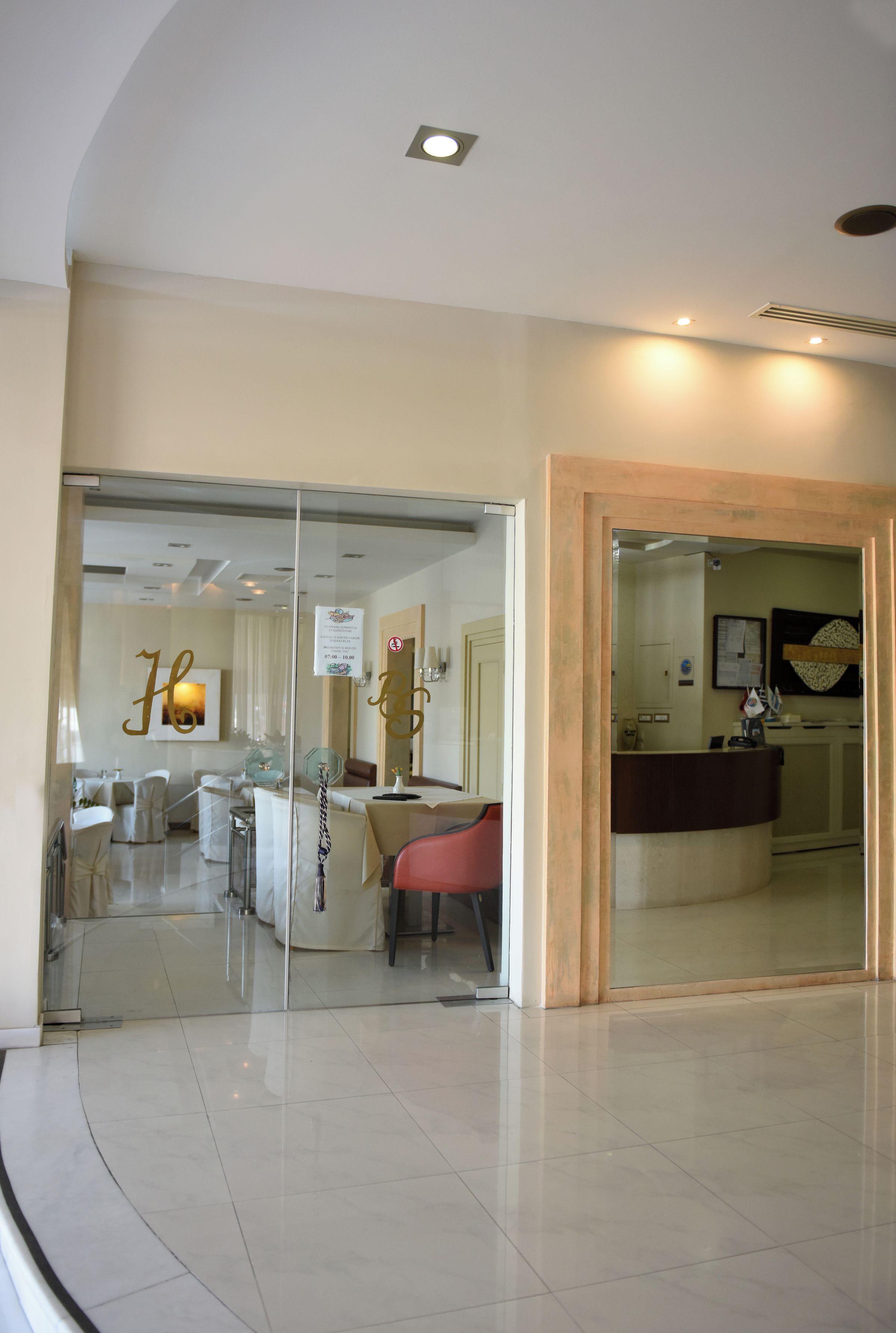 A hotel lobby with a reception desk, a dining area with chairs, and a glass partition.