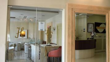 A hotel lobby with a reception desk, a dining area with chairs, and a glass partition.