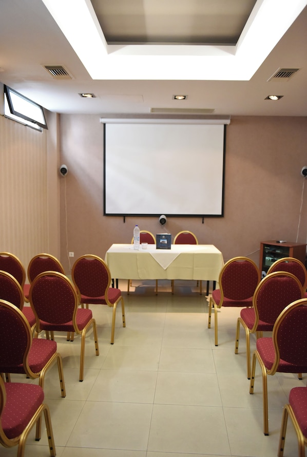 Una sala conferenze con un grande schermo, un tavolo con un portatile e file di sedie rosse.