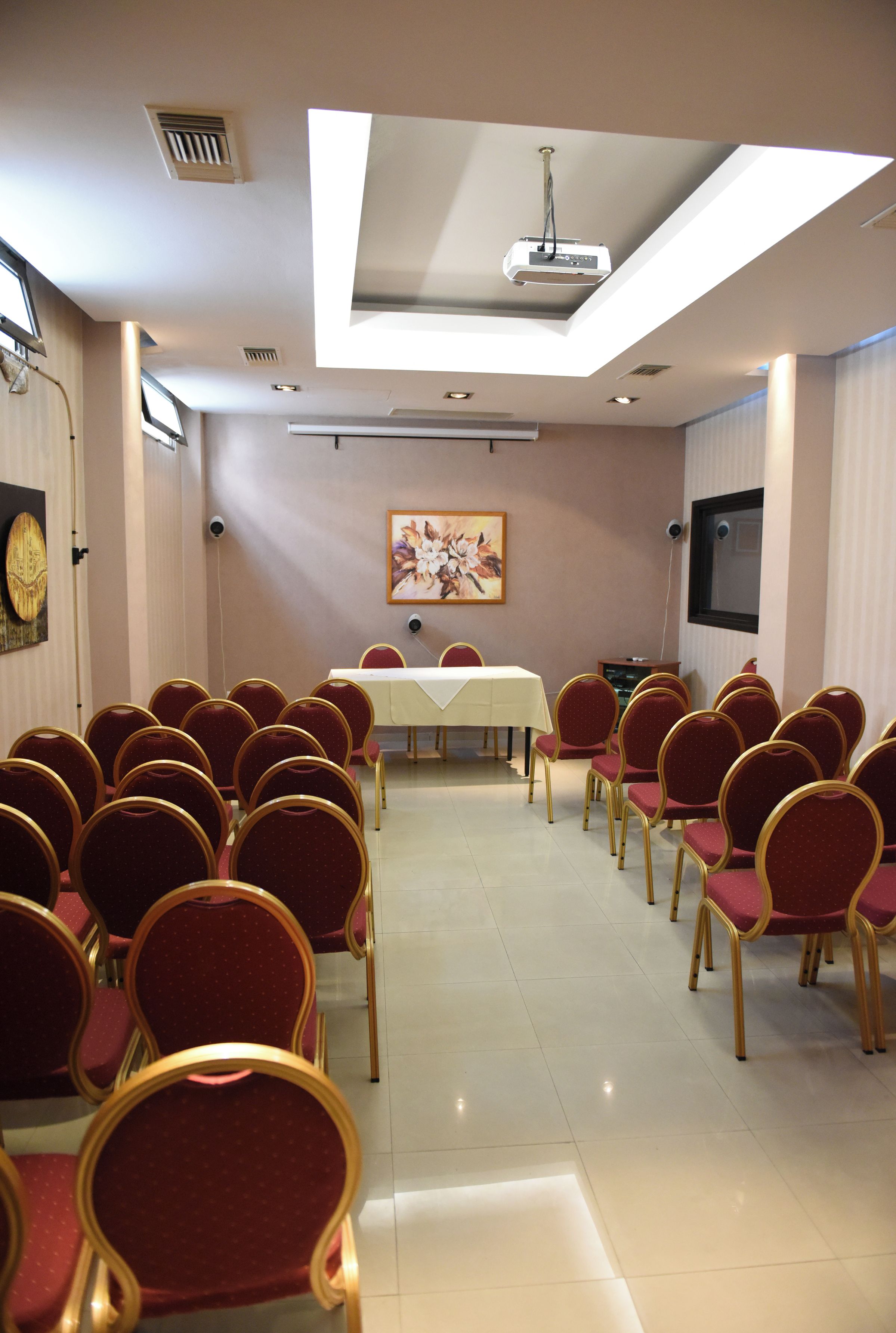A conference room with a long table, rows of red chairs, a projector, and a clock on the wall.