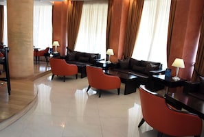 Una hall d'albergo moderna con divani, poltrone rosse e un tavolino da caffè.