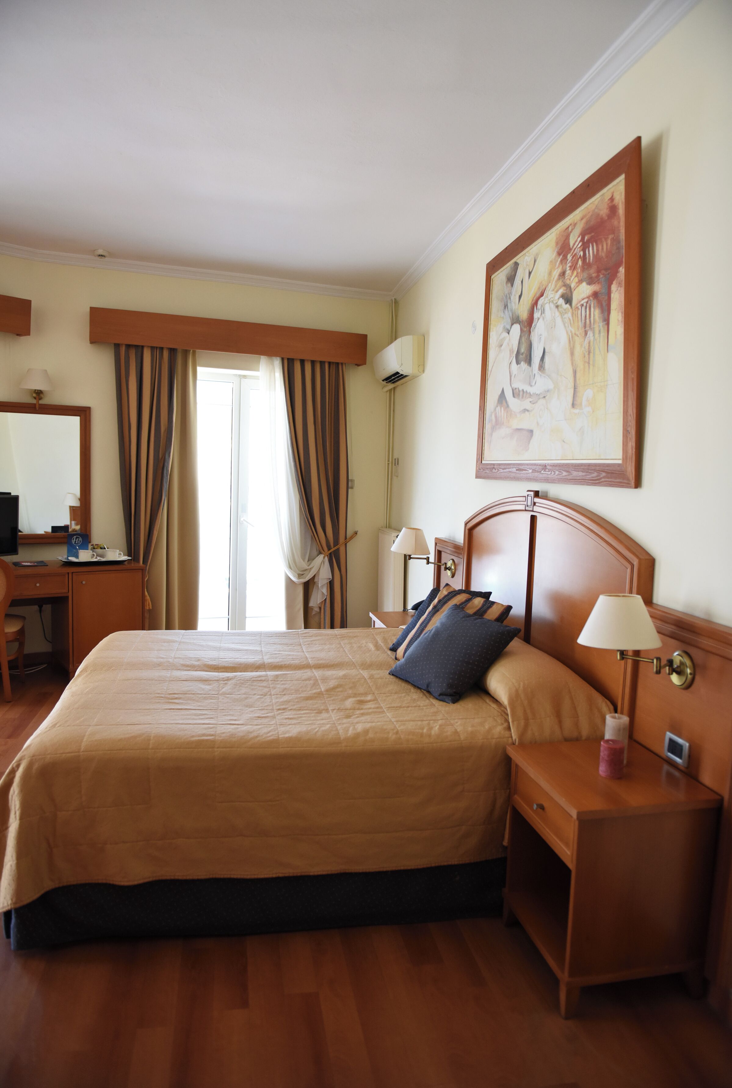 A hotel room with a large bed, bedside tables, a desk, a chair, and a painting on the wall.