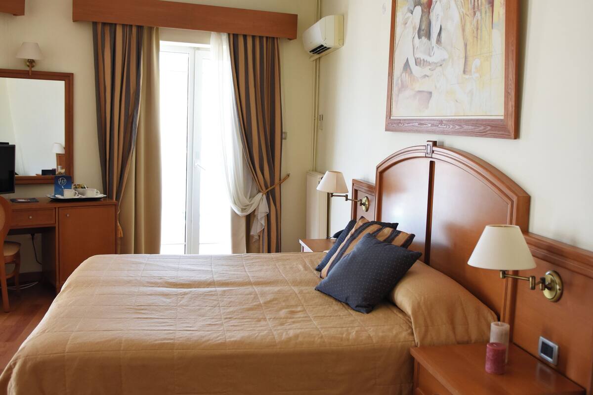 A hotel room with a large bed, bedside tables, a desk, a chair, and a painting on the wall.
