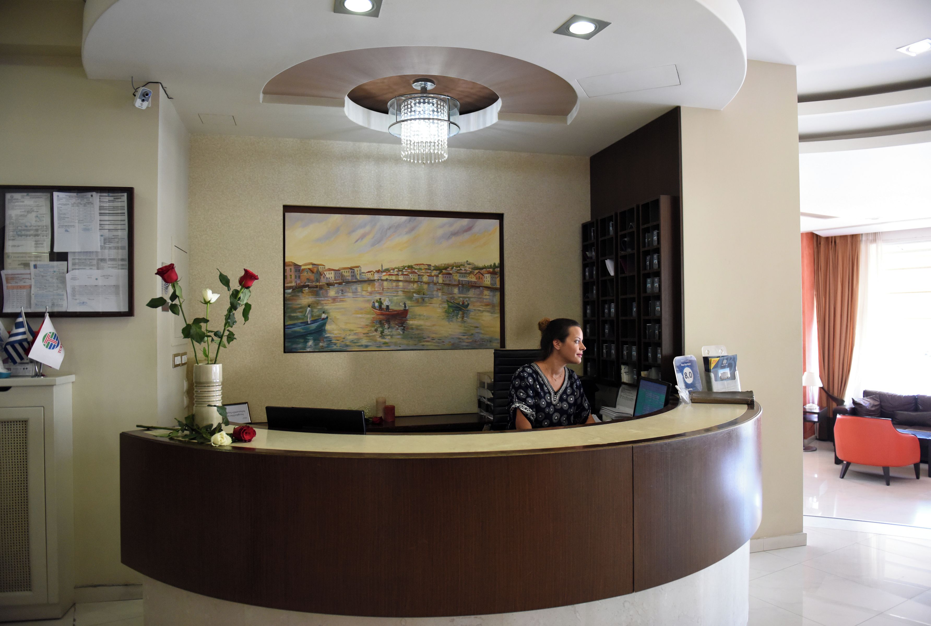A reception desk with a painting, a vase with flowers, and a computer.