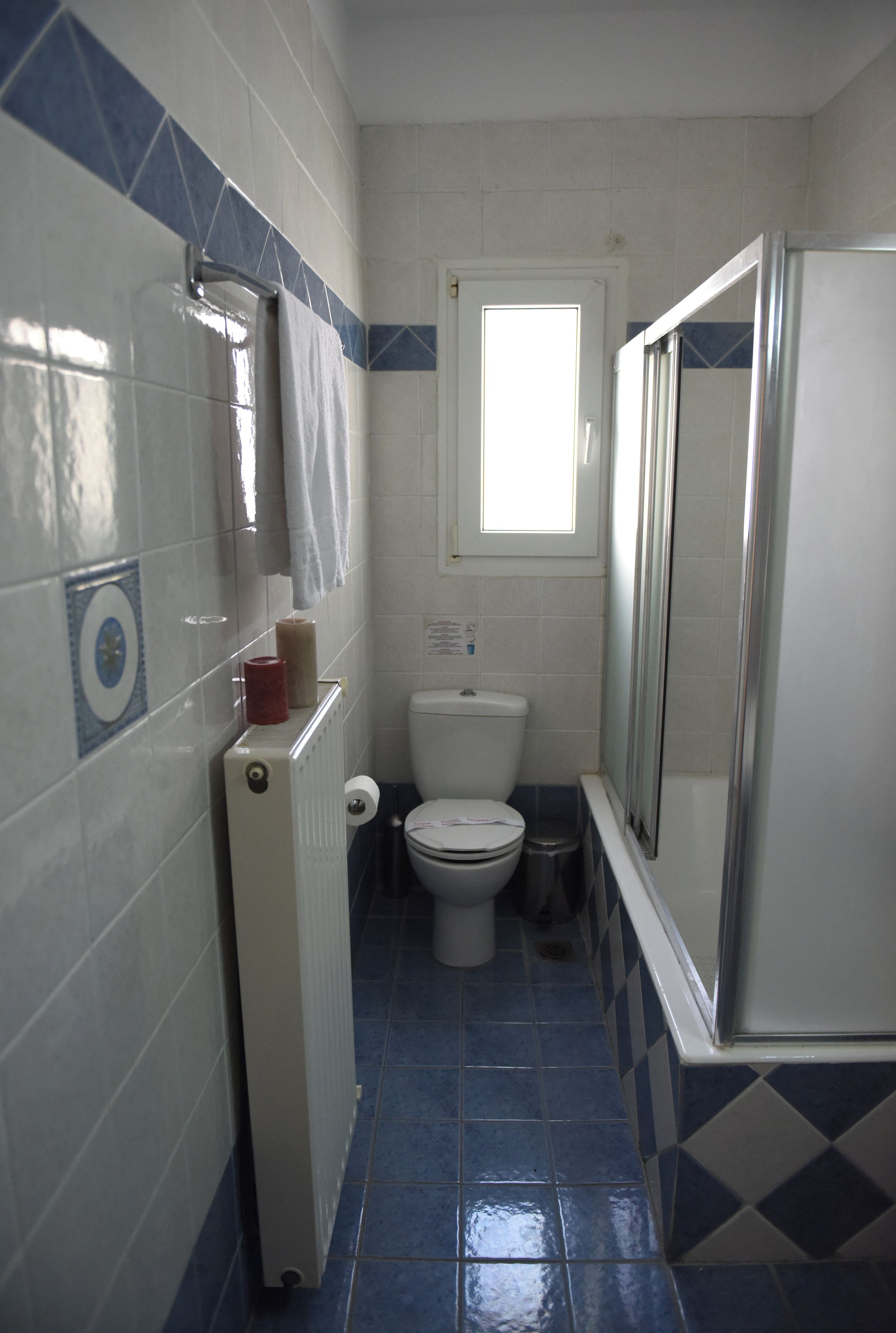 Un baño pequeño con inodoro, radiador, ventana y zona de ducha.