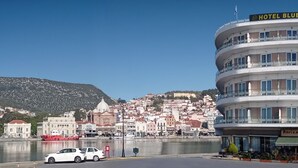 Un hôtel à plusieurs étages, doté de balcons, offrant une vue sur une ville historique et donnant sur un plan d’eau au premier plan.