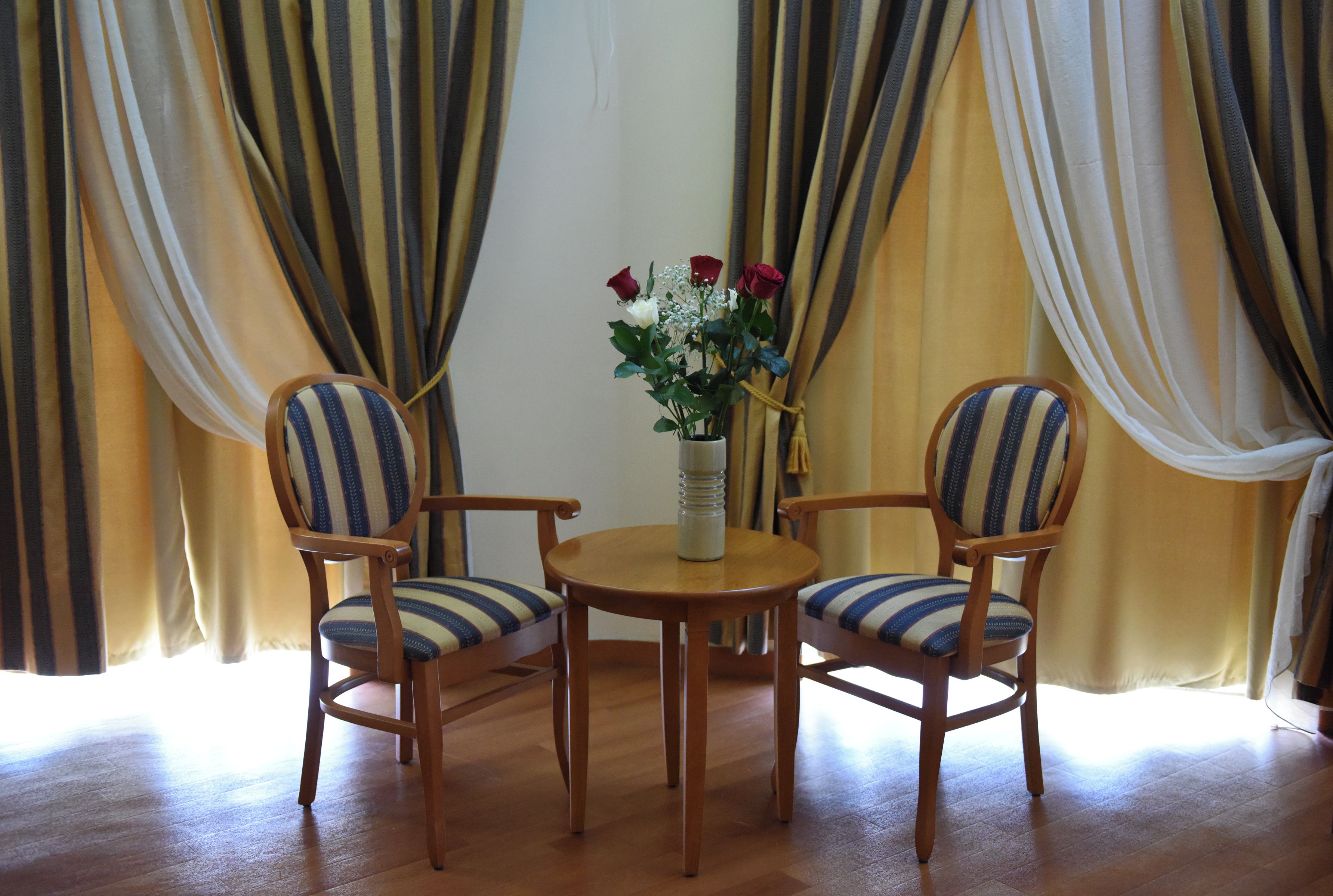A room with a wooden table and two striped chairs, a vase with flowers, and curtains.