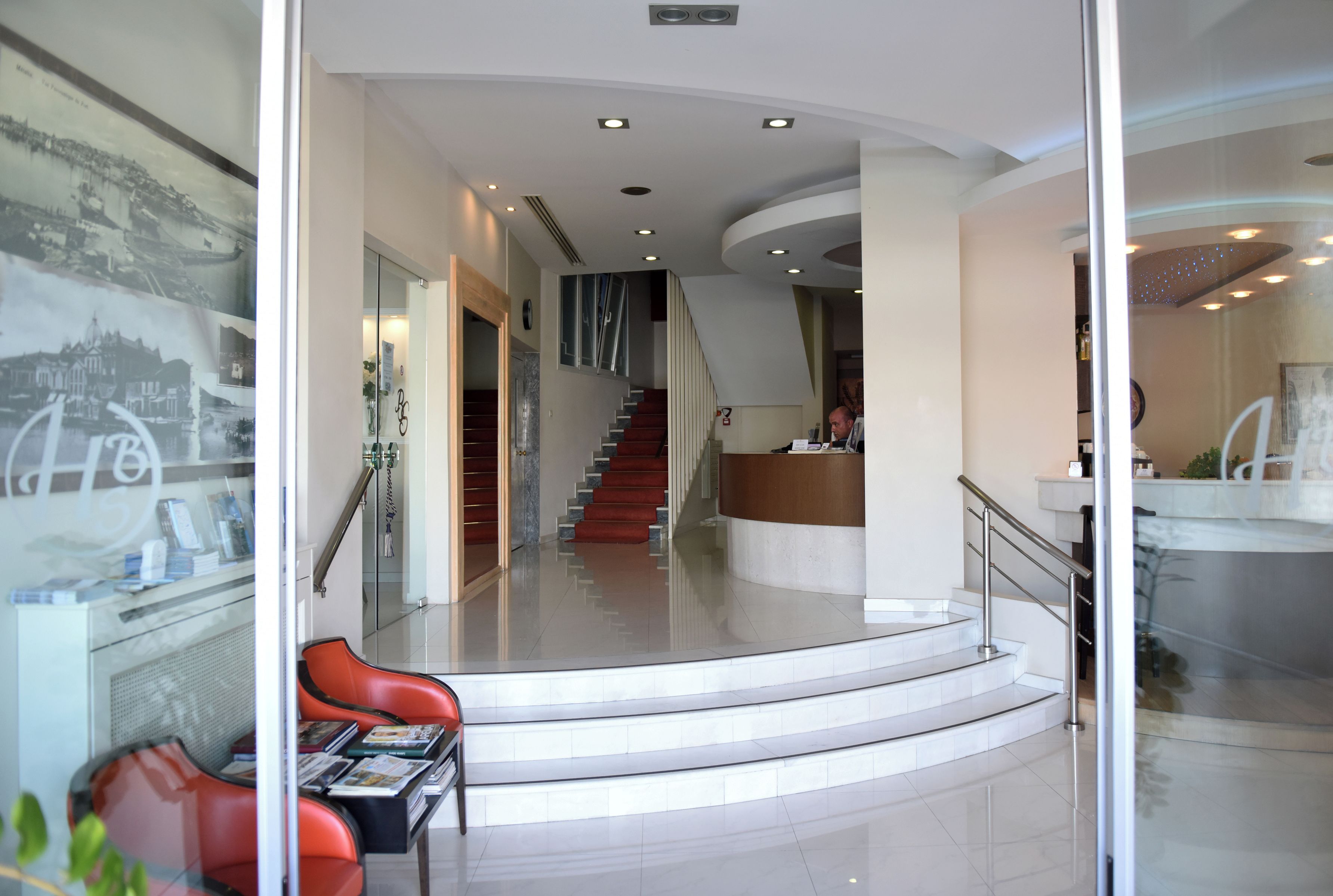 A modern hotel lobby with a reception desk, a staircase, and seating area.