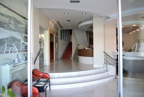 A modern hotel lobby with a reception desk, a staircase, and seating area.