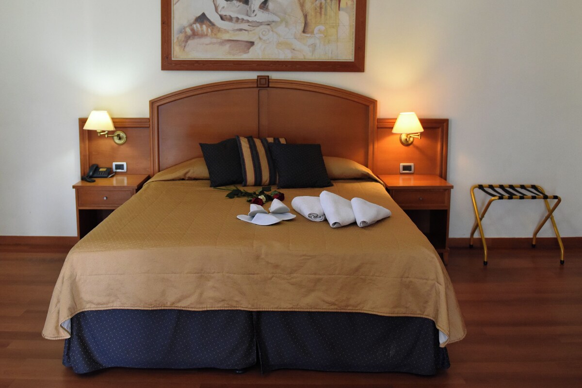 Une chambre d’hôtel avec un grand lit, deux tables de chevet avec des lampes, une tête de lit en bois et un tableau au-dessus du lit.