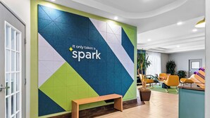 A modern lobby with a geometric wall design, a wooden bench, and a reception desk. - Spark by Hilton San Antonio near SeaWorld (San Antonio)