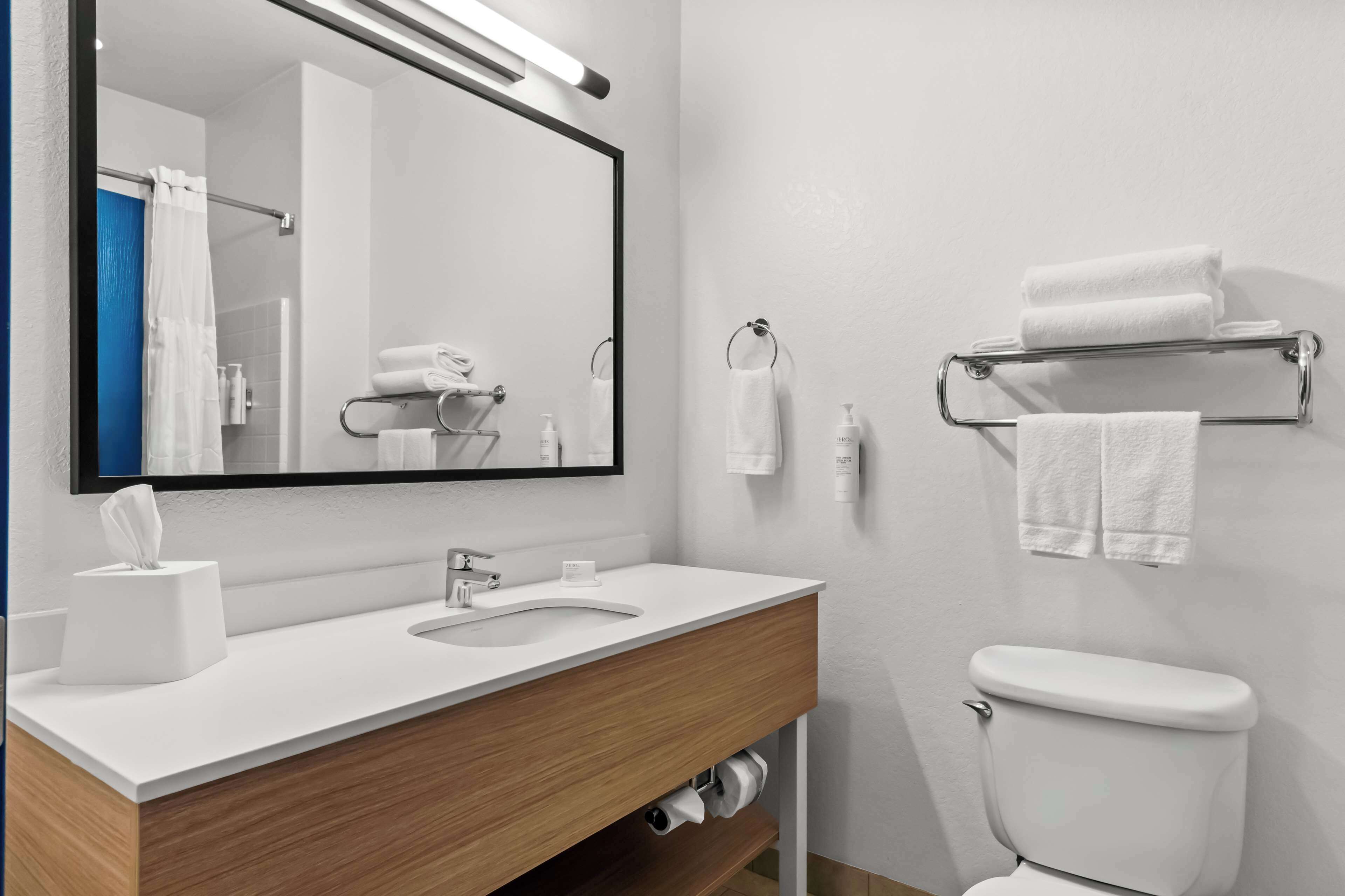 A modern bathroom with a white sink, a mirror, a toilet, and a towel rack.