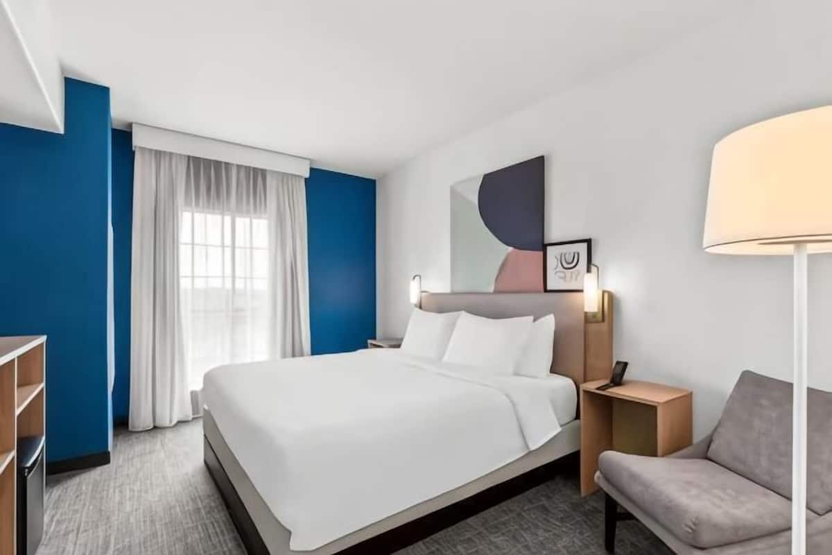 A hotel room with a large bed, a desk, a chair, a lamp, and a window with curtains.