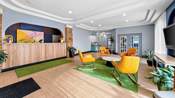 A modern lobby with a reception desk, yellow chairs, a round table, and potted plants. - Spark by Hilton San Antonio near SeaWorld (San Antonio)
