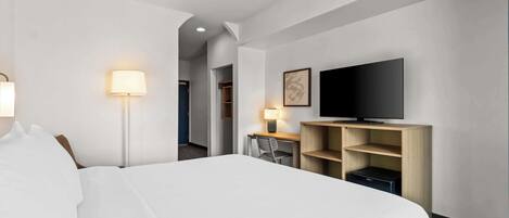 Una habitación de hotel con una cama grande, un escritorio con una silla, un televisor y una lámpara.
