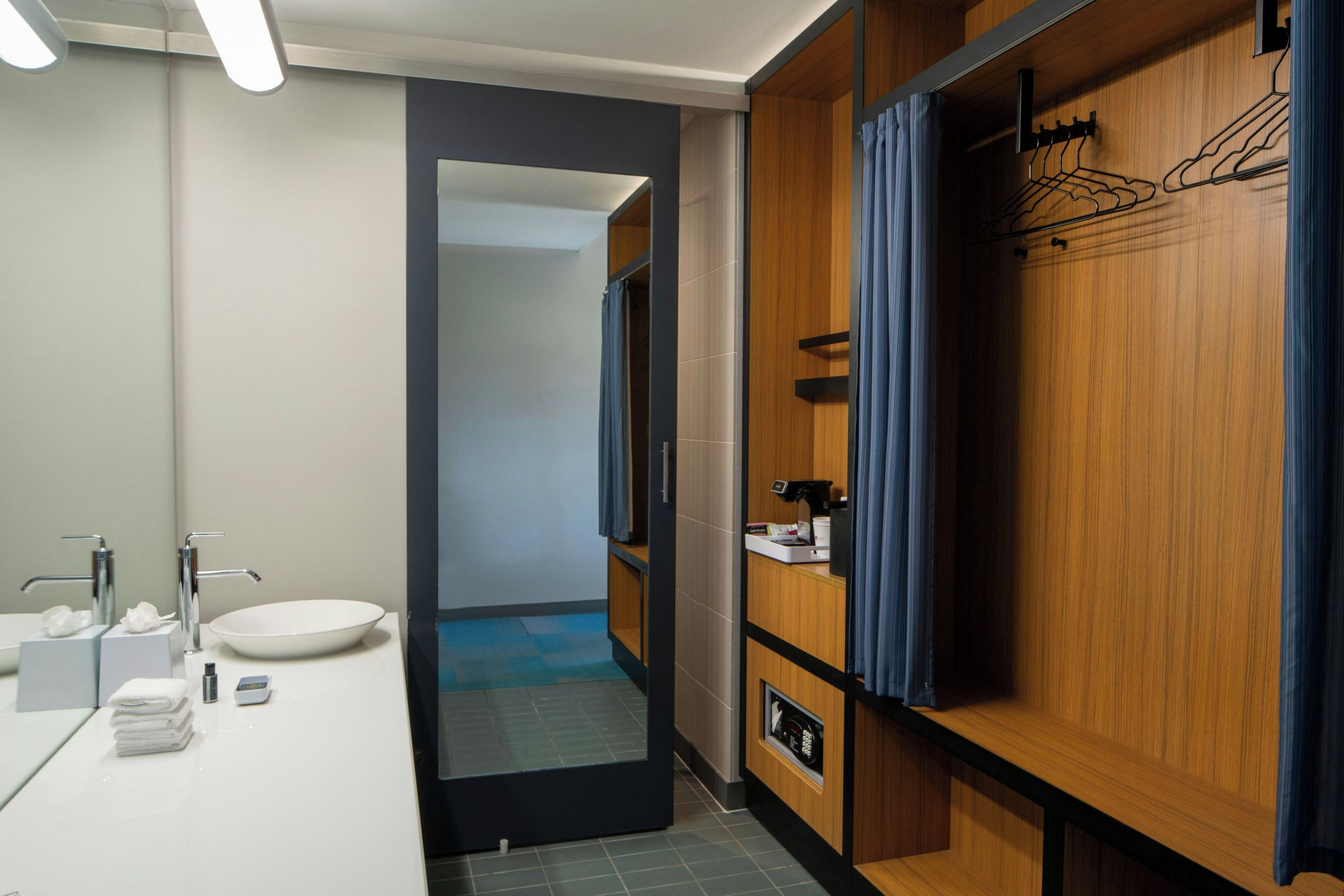 A modern bathroom with a white sink, two faucets, a mirror, and a wooden vanity with a towel rack.