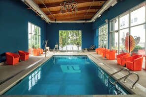 An indoor swimming pool with blue water, surrounded by orange chairs, large windows, and a wooden ceiling. - Aloft by Marriott Green Bay (Green Bay)
