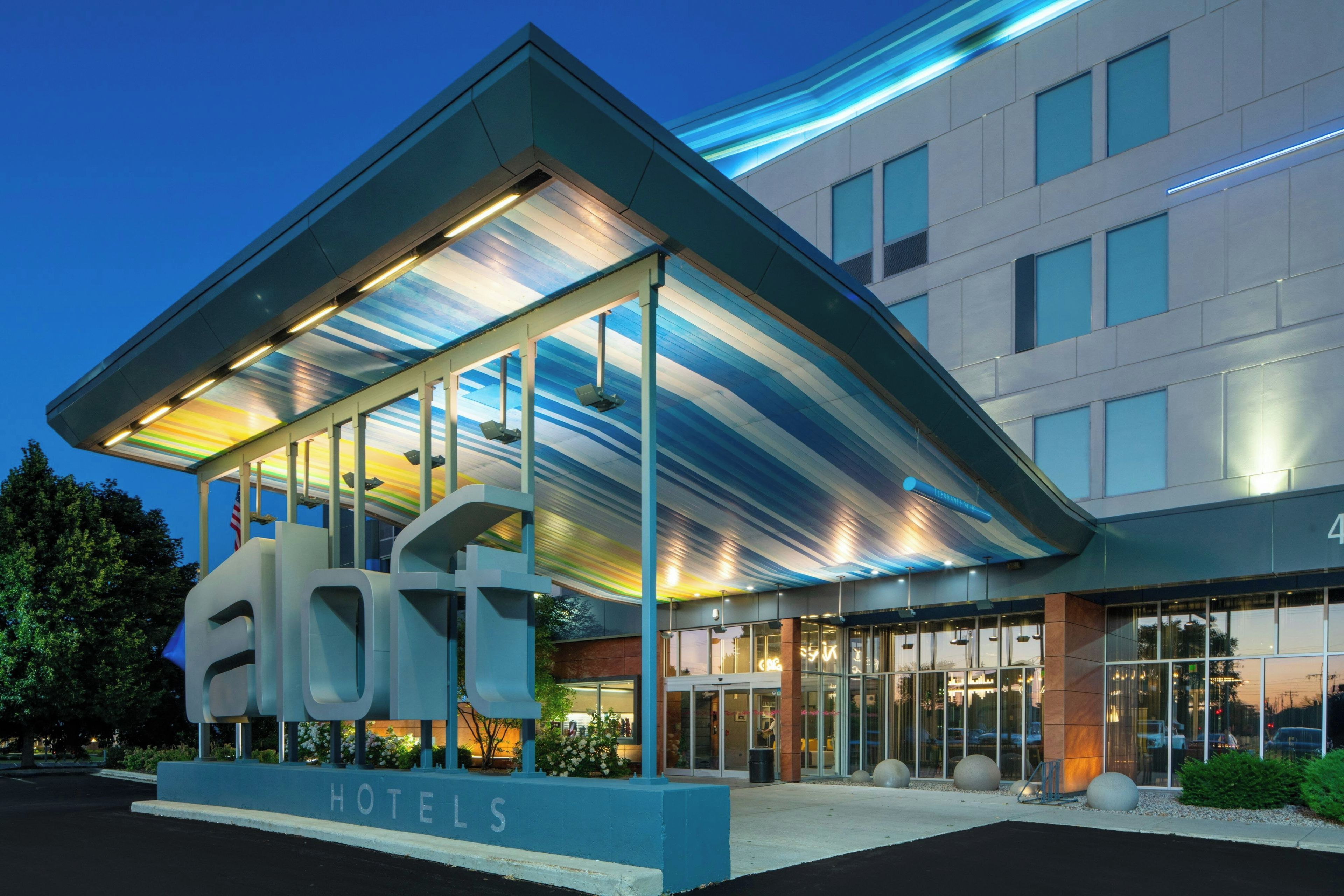 A modern hotel with a prominent 'HOTELS' sign, large windows, and a covered entrance area.