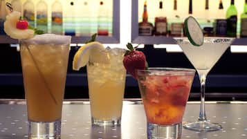 Three cocktails on a bar counter with a background of various bottles.