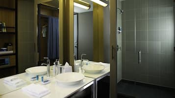 A hotel bathroom with two sinks, a large mirror, and a shower area.
