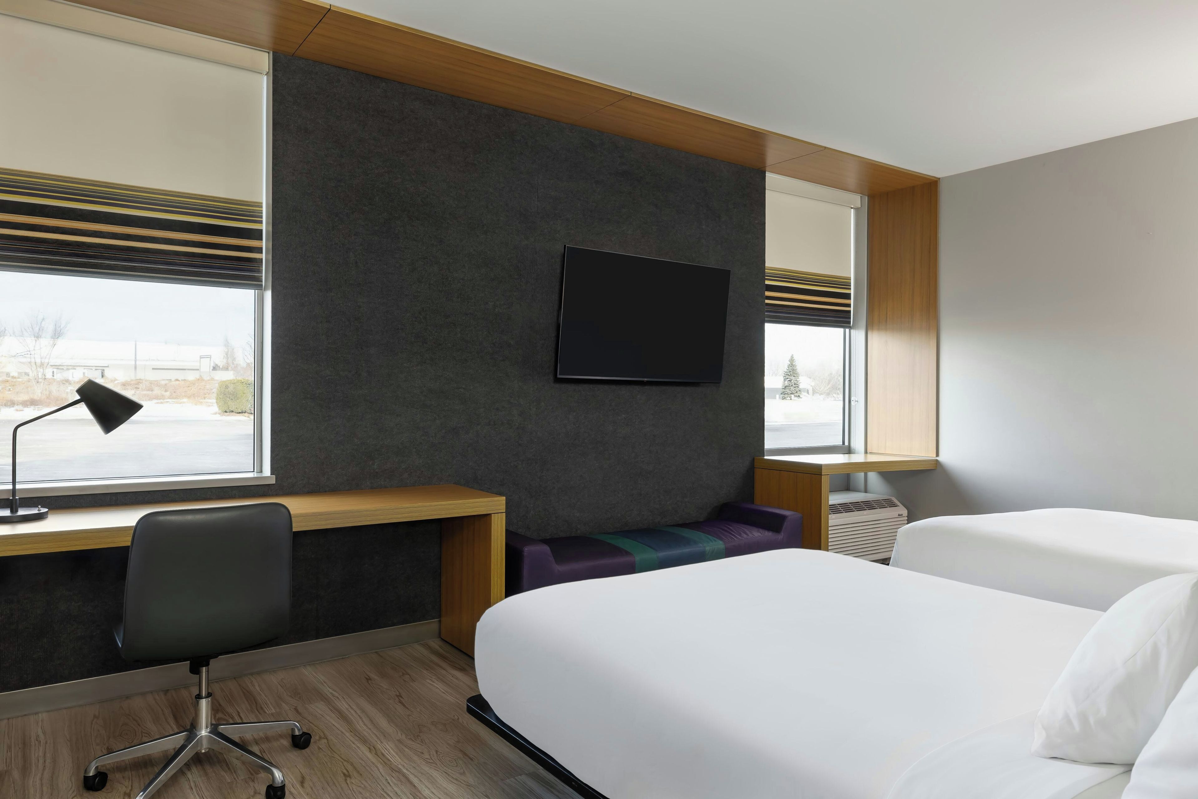 Habitación de hotel con escritorio, dos camas, televisor y ventana con persianas.
