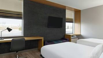 Habitación de hotel con escritorio, dos camas, televisor y ventana con persianas.