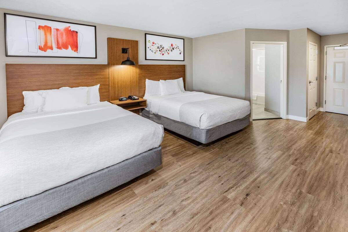 A hotel room with two beds, wooden headboards, a nightstand, and artwork on the walls.
