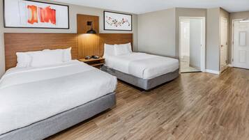 Habitación de hotel con dos camas, cabeceros de madera, una mesita de noche y obras de arte en las paredes.
