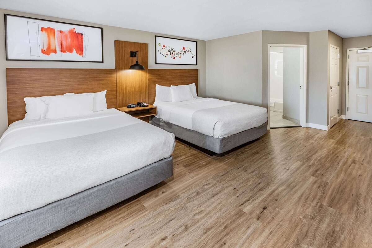 A hotel room with two beds, a wooden headboard, a nightstand, and a wall-mounted lamp.