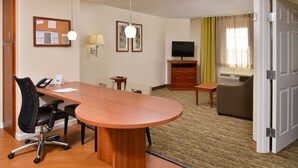 Quarto de hotel com escrivaninha de madeira, cadeira de escritório, televisão, sofá e cama.
