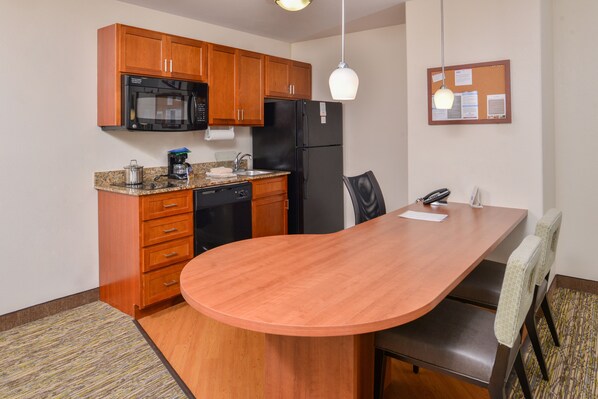 A compact kitchen with wooden cabinets, a black refrigerator, a microwave, and a coffee maker. - Candlewood Suites ABILENE by IHG (Abilene)