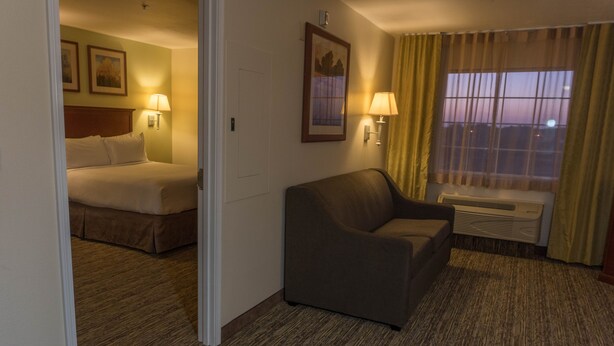 Quarto de hotel com cama, sofá, janela com cortinas e luminárias fixadas na parede.