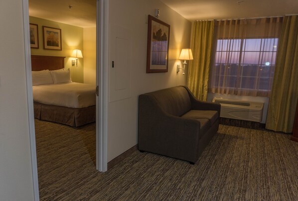 A hotel room with a bed, a sofa, a window with curtains, and wall-mounted lamps. - Candlewood Suites ABILENE by IHG (Abilene)