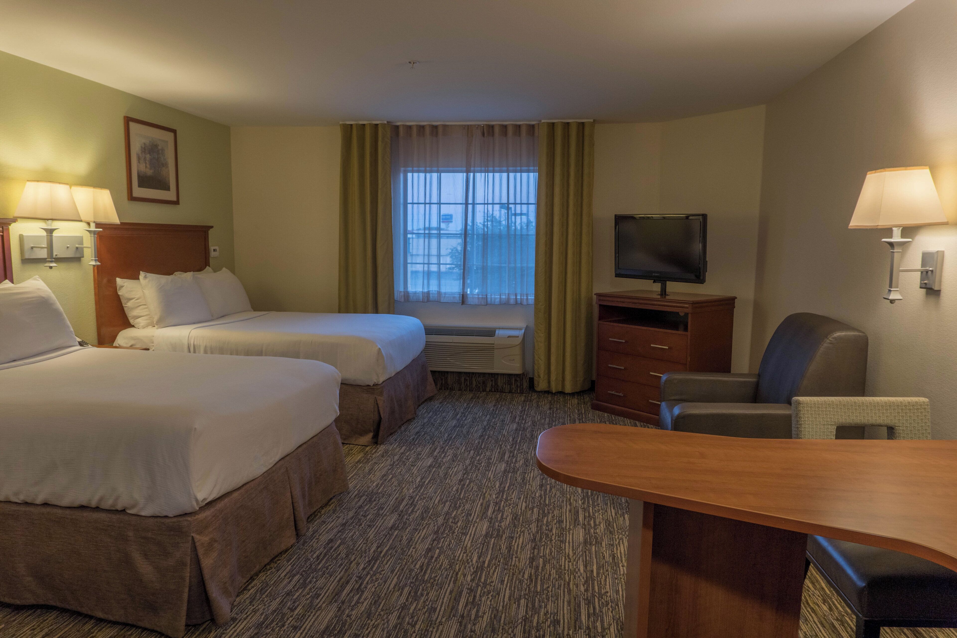 A hotel room with two beds, a television, a desk, and a chair.