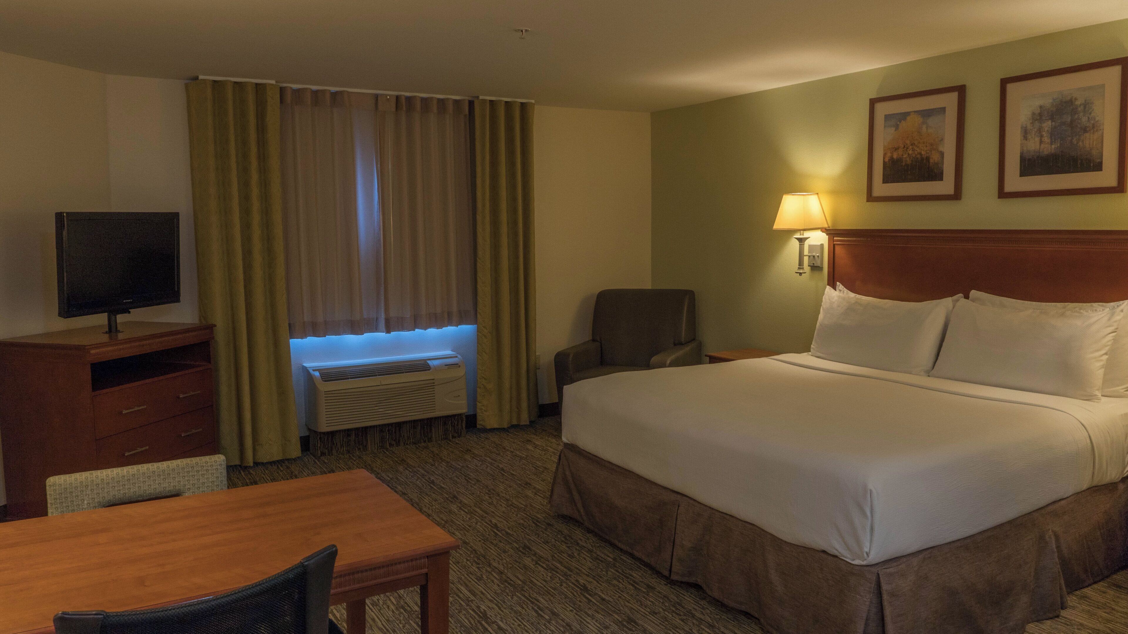 A hotel room with a bed, a desk, a chair, a television, a lamp, and a window with curtains.