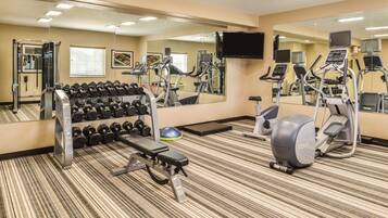 A gym with exercise equipment, a bench, and a mirror.