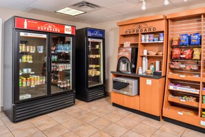A self-service breakfast area with refrigerated beverage dispensers, a coffee machine, and shelves stocked with snacks and breakfast items. - Candlewood Suites ABILENE by IHG (Abilene)