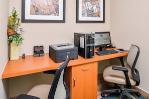 A hotel office desk with a desktop computer, printer, and two chairs.