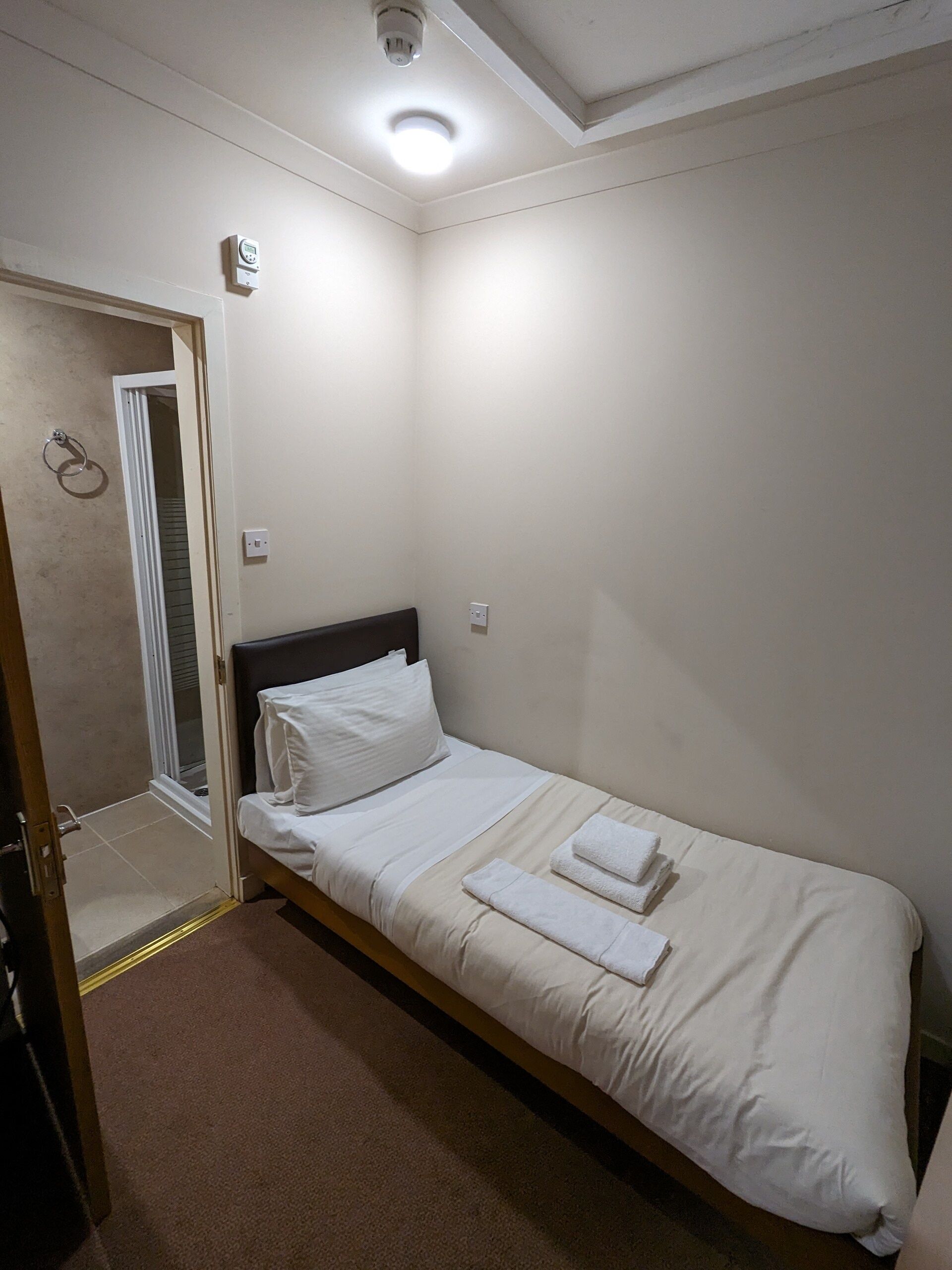 A single-bed room with a wooden headboard, white bedding, and a pair of towels on the bed.