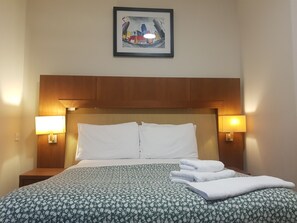 A hotel room with a bed, two bedside lamps, a framed artwork on the wall, and a neatly folded towel on the bed. - Aberdeen House (Aberdeen)