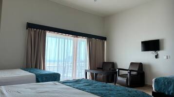 A hotel room with two beds, a desk, a chair, a TV, and a large window with curtains.