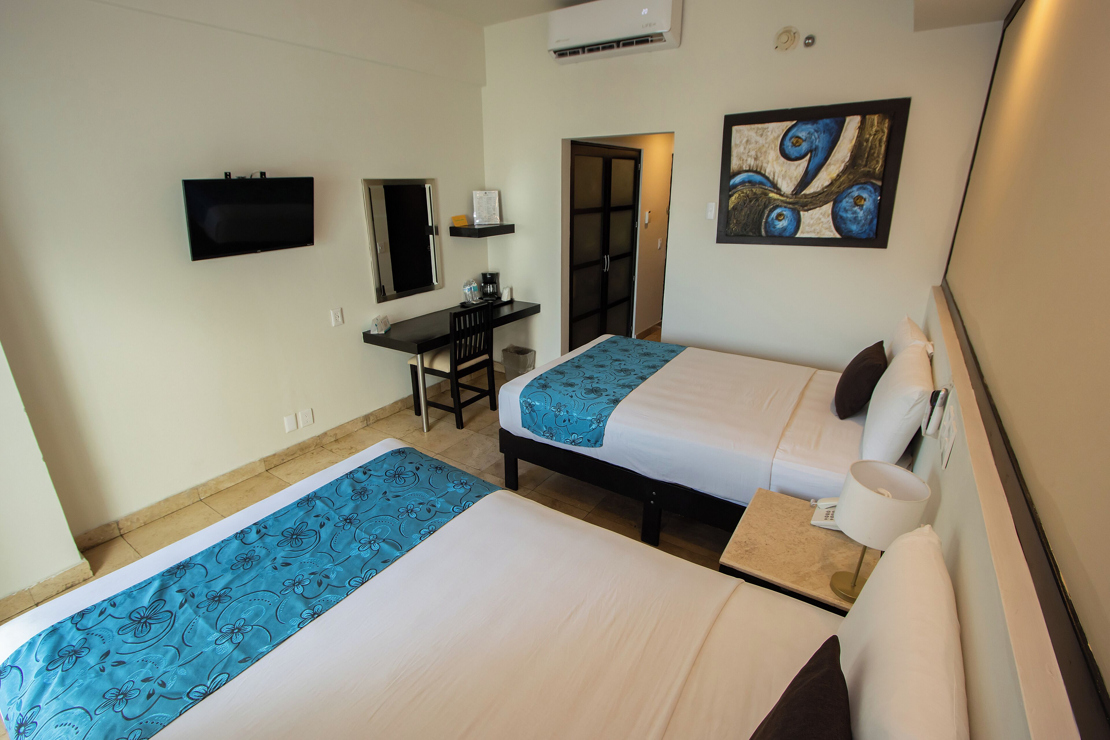 A hotel room with two beds, a desk, a TV, and a painting on the wall.