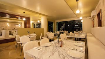 Un espace repas moderne avec des tables en marbre, des chaises blanches et des luminaires suspendus.