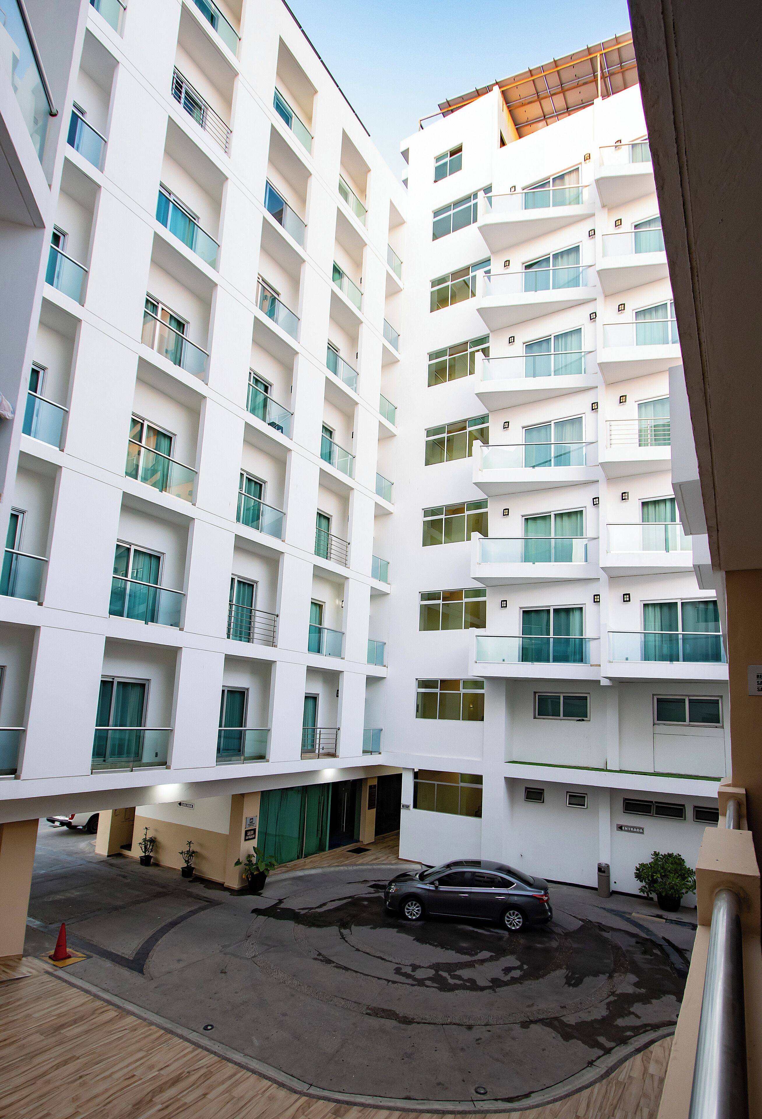 A multi-story hotel with balconies, a parking area, and a green entrance.