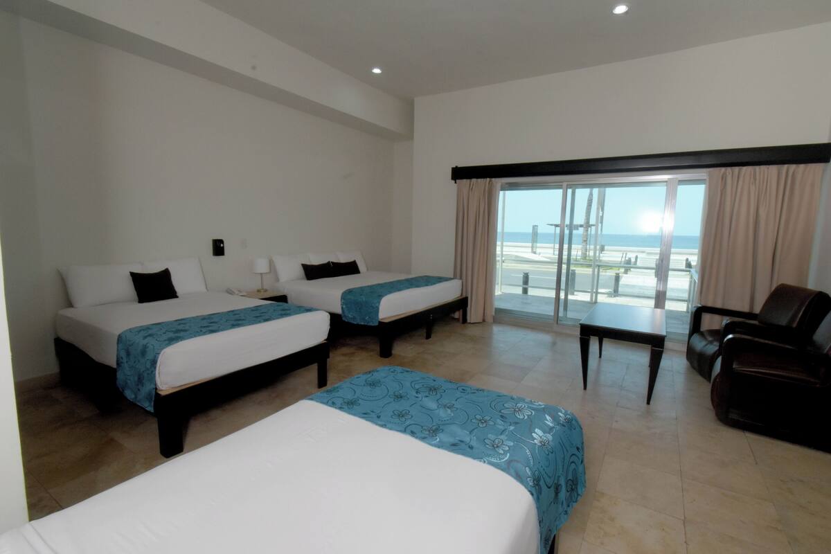 A hotel room with two beds, a balcony with a view, a desk, and a leather chair.