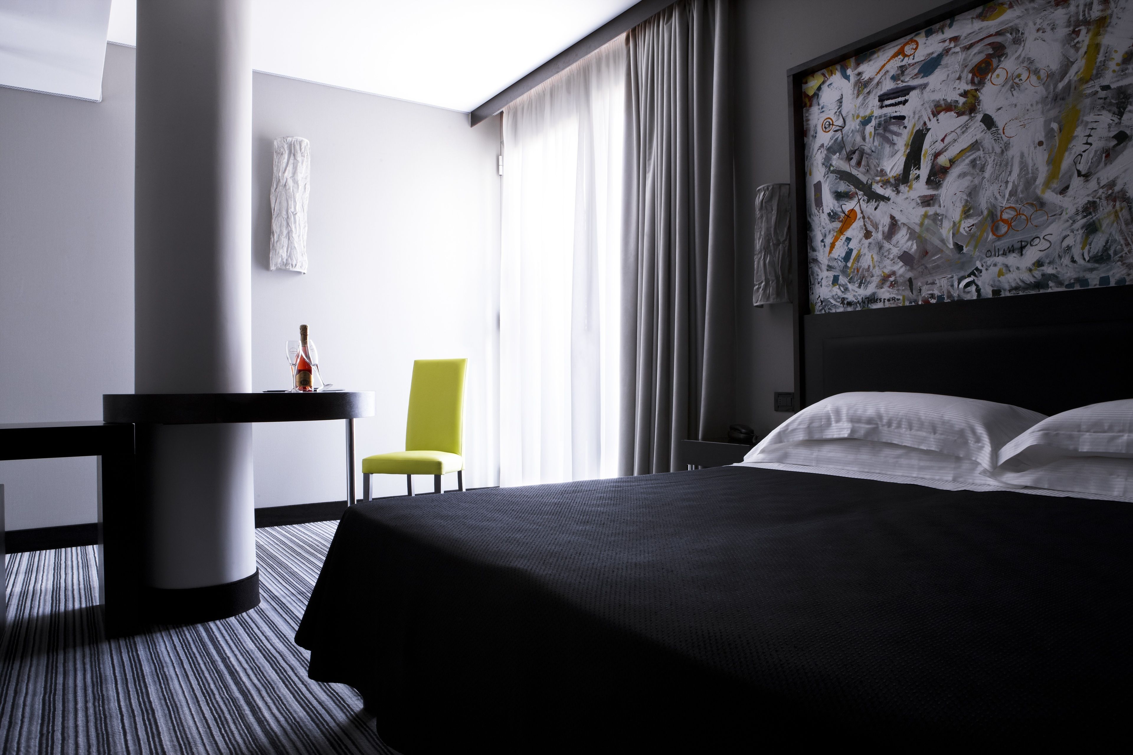 A hotel room with a large bed, a desk, a chair, and a painting on the wall.